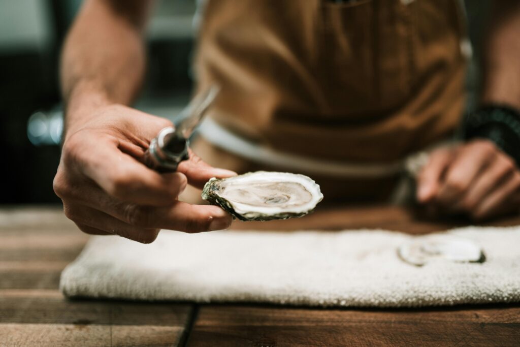Close-up of chef's hand shucking an oyster on a wooden table in the kitchen.